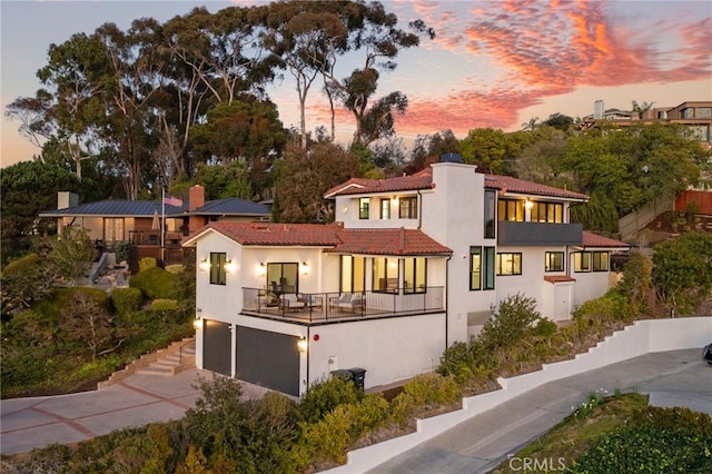 rear view of property featuring stucco siding, a balcony, a garage, driveway, and a tiled roof