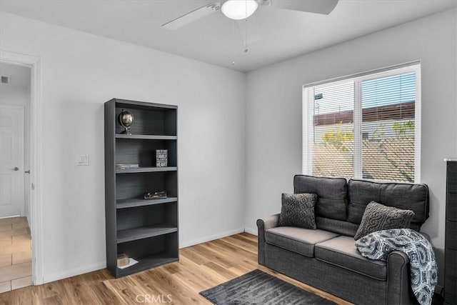 sitting room featuring built in shelves, a ceiling fan, light wood-style floors, and baseboards