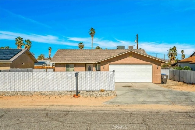 ranch-style house featuring a fenced front yard, concrete driveway, an attached garage, and stucco siding