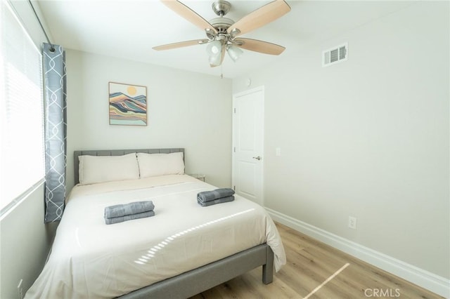 bedroom featuring light wood-style flooring, a ceiling fan, visible vents, and baseboards