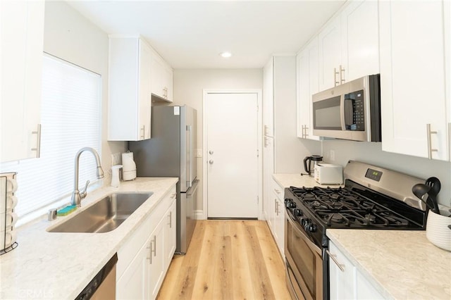 kitchen featuring appliances with stainless steel finishes, white cabinetry, a sink, and light wood-style flooring