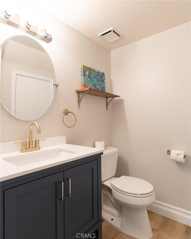 half bathroom featuring baseboards, visible vents, toilet, wood finished floors, and vanity