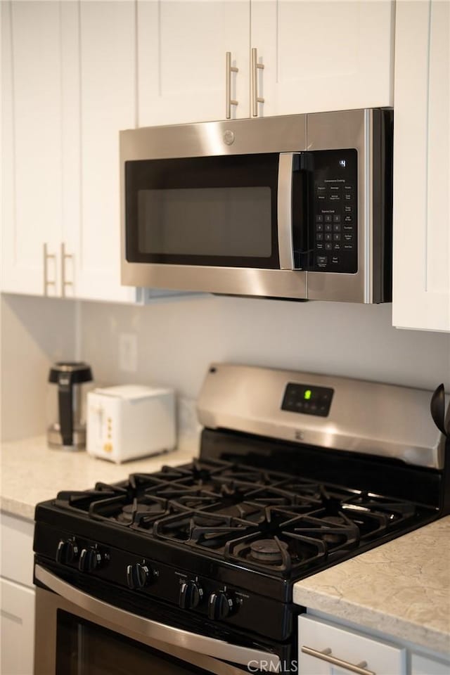 kitchen with stainless steel appliances, white cabinets, and light stone countertops