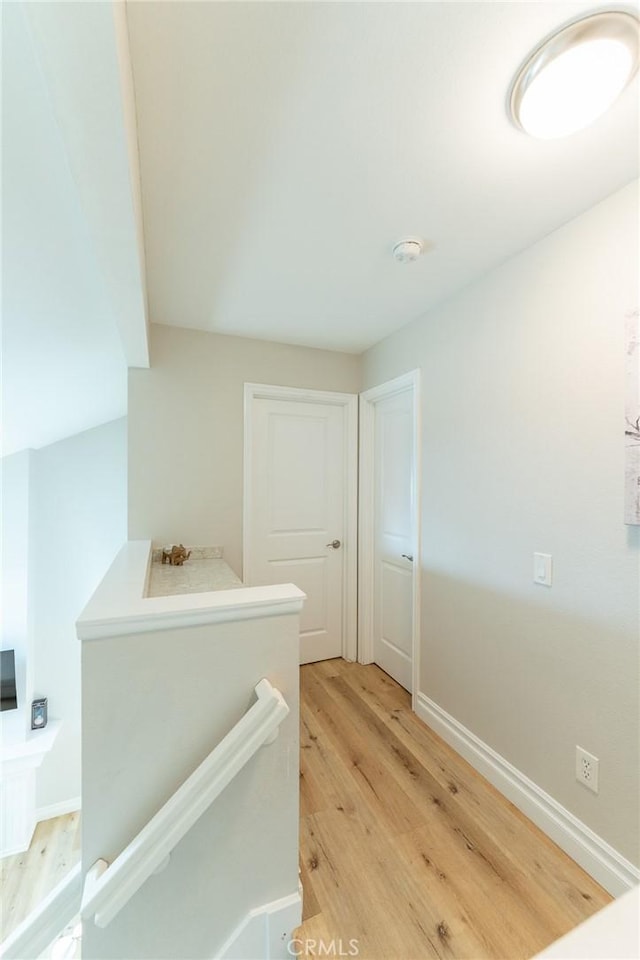 hallway with light wood finished floors, baseboards, and an upstairs landing