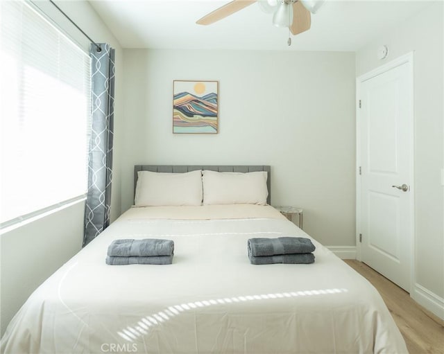 bedroom featuring a ceiling fan, baseboards, multiple windows, and light wood finished floors