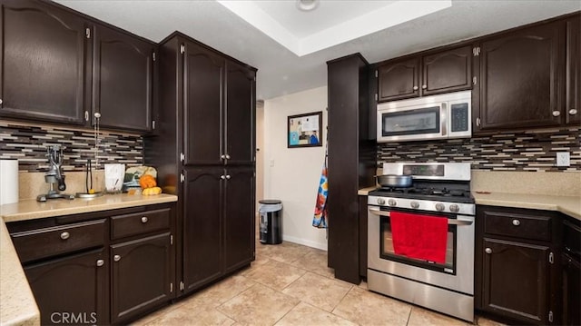 kitchen featuring light tile patterned floors, tasteful backsplash, stainless steel appliances, dark brown cabinets, and light countertops