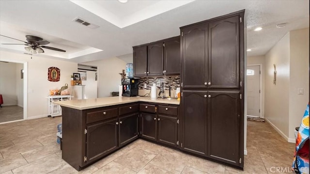 kitchen featuring a peninsula, visible vents, light countertops, dark brown cabinets, and a tray ceiling