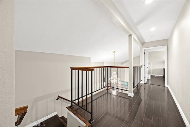 corridor featuring a chandelier, wood tiled floor, baseboards, and an upstairs landing