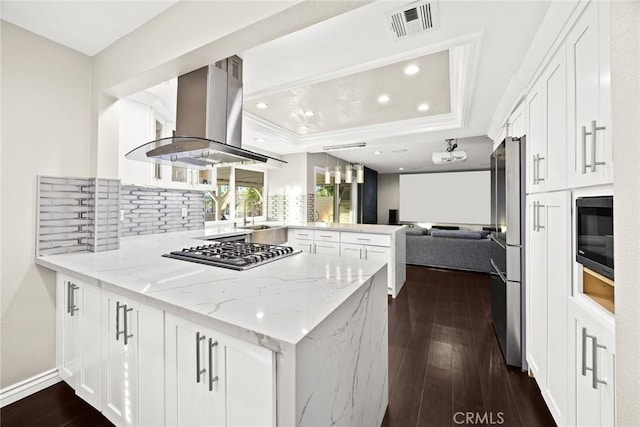 kitchen with island range hood, appliances with stainless steel finishes, open floor plan, light stone counters, and a peninsula