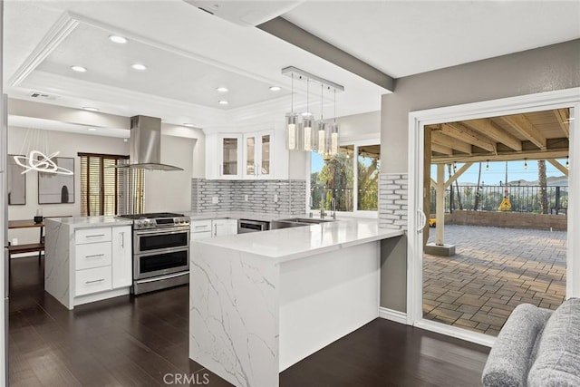 kitchen with appliances with stainless steel finishes, glass insert cabinets, a peninsula, white cabinetry, and pendant lighting