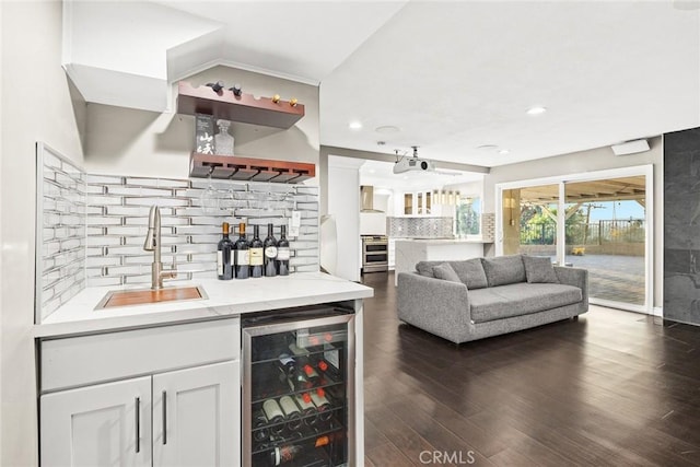 bar with dark wood-style floors, wall chimney exhaust hood, wine cooler, wet bar, and a sink