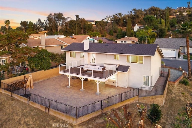 back of property at dusk with a patio, a chimney, stucco siding, a residential view, and a fenced backyard