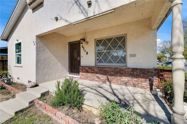 doorway to property featuring brick siding, crawl space, and stucco siding