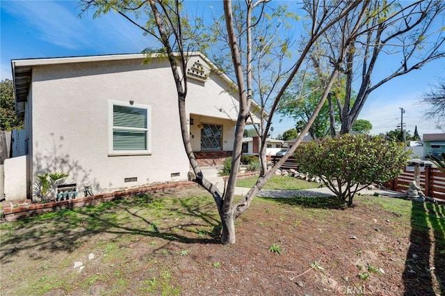 view of home's exterior featuring crawl space, fence, a lawn, and stucco siding