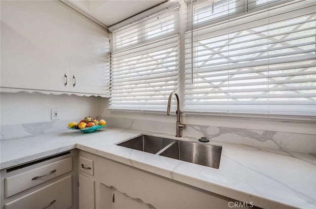 kitchen with light stone counters, a sink, and white cabinets