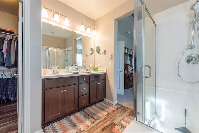 bathroom featuring a sink, wood finished floors, a spacious closet, double vanity, and a stall shower