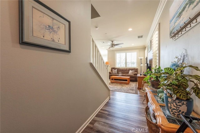 corridor with dark wood-type flooring, visible vents, baseboards, ornamental molding, and stairway