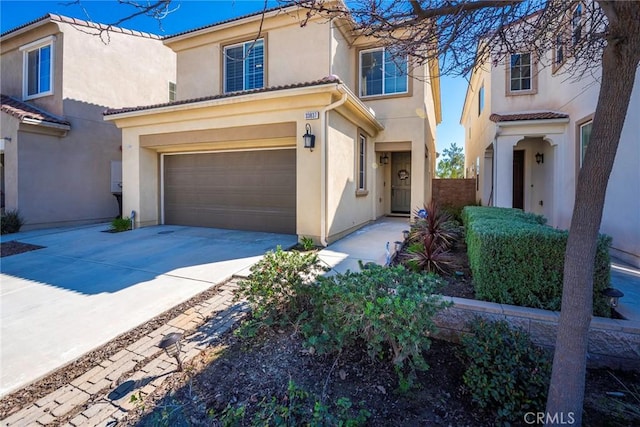 mediterranean / spanish-style home featuring an attached garage, a tile roof, concrete driveway, and stucco siding