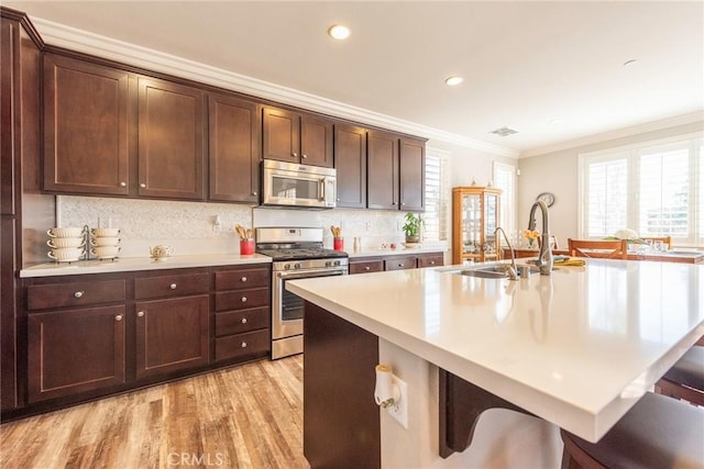 kitchen with appliances with stainless steel finishes, light countertops, ornamental molding, and a breakfast bar area