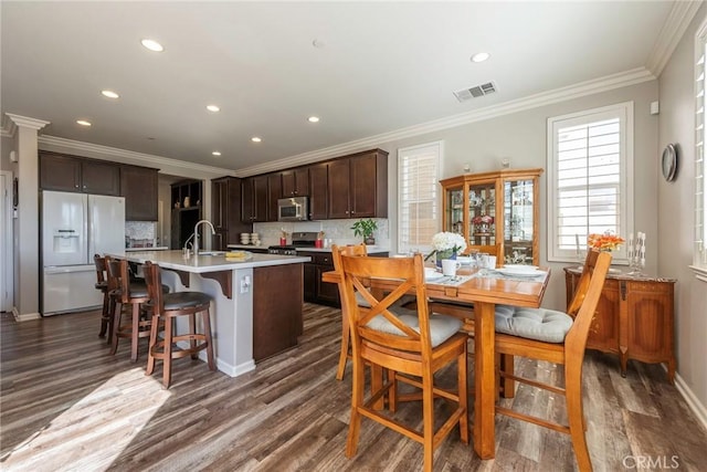 kitchen with white refrigerator with ice dispenser, visible vents, light countertops, stainless steel microwave, and an island with sink