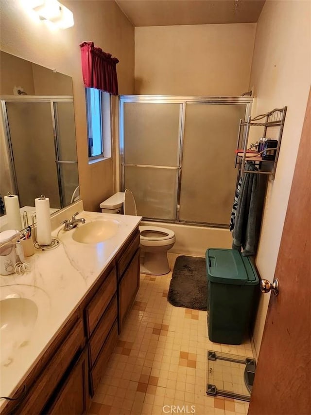 full bathroom with double vanity, shower / bath combination with glass door, a sink, and toilet