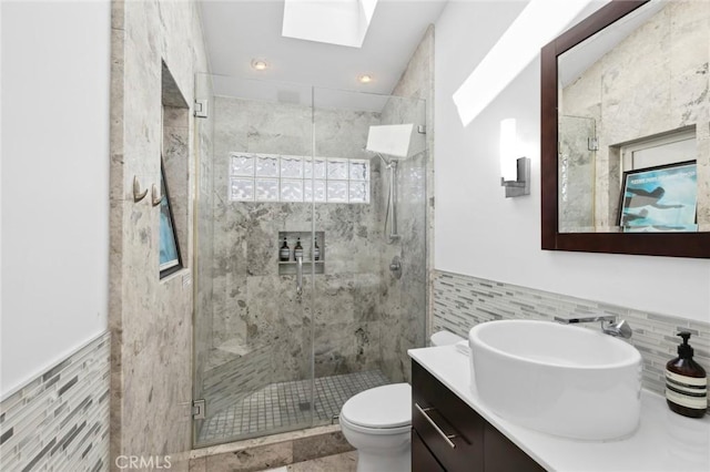 bathroom with a shower stall, toilet, vanity, a skylight, and tile walls