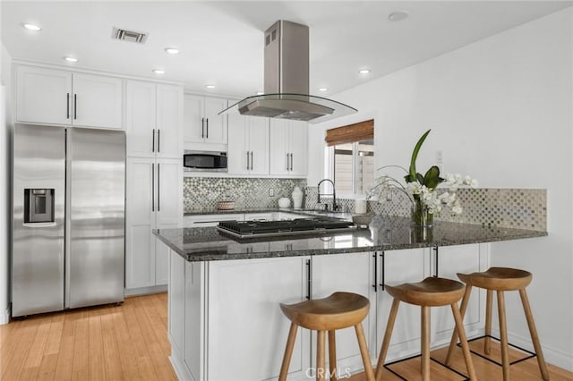 kitchen with visible vents, a peninsula, dark stone counters, island exhaust hood, and stainless steel appliances