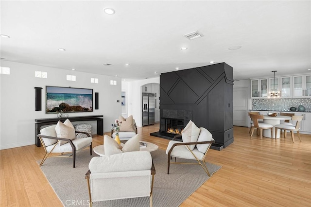 living area featuring light wood-style flooring, arched walkways, visible vents, and a large fireplace