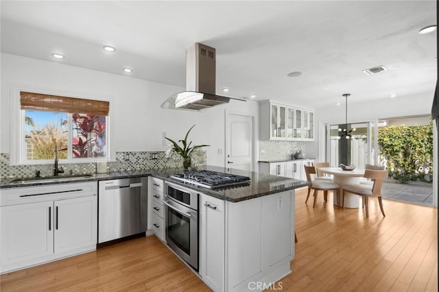 kitchen featuring a sink, white cabinetry, appliances with stainless steel finishes, a peninsula, and island range hood