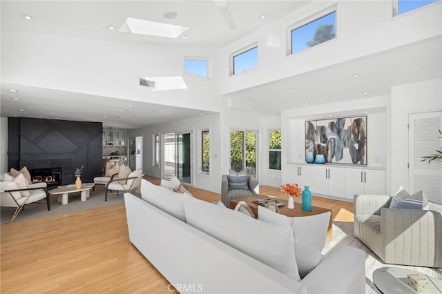 living area featuring light wood finished floors, visible vents, a large fireplace, recessed lighting, and a skylight