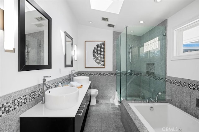 bathroom with visible vents, a shower stall, a wainscoted wall, tile walls, and a sink