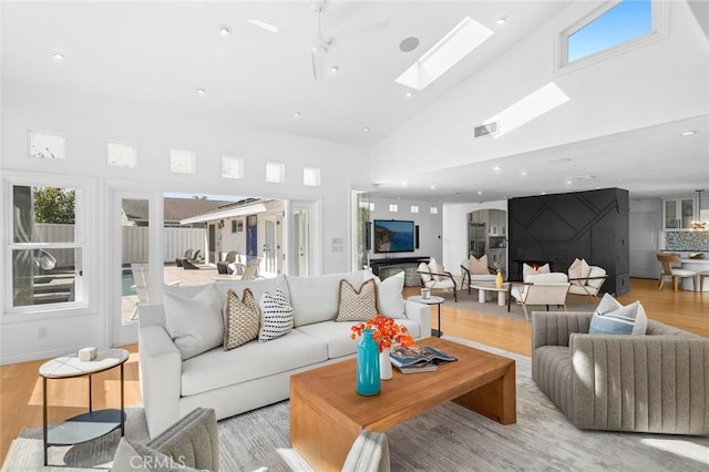 living room with a skylight, wood finished floors, visible vents, and high vaulted ceiling