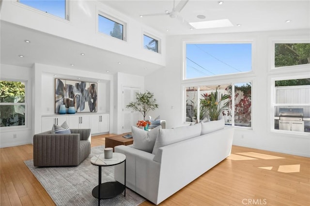 living area with a healthy amount of sunlight, a skylight, light wood-style floors, and a towering ceiling