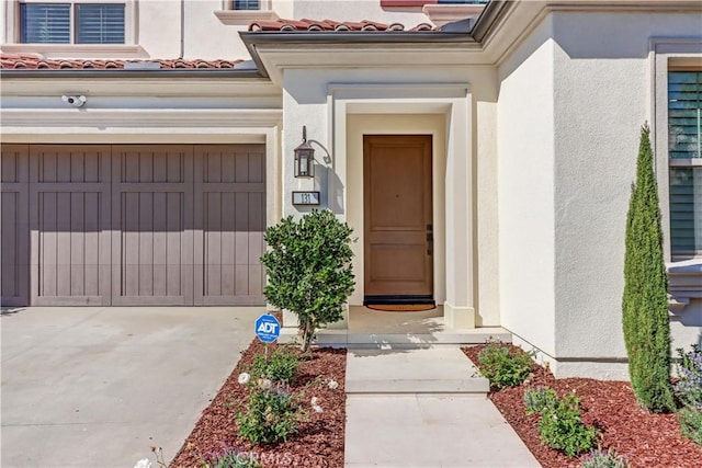 property entrance with a garage, concrete driveway, a tile roof, and stucco siding