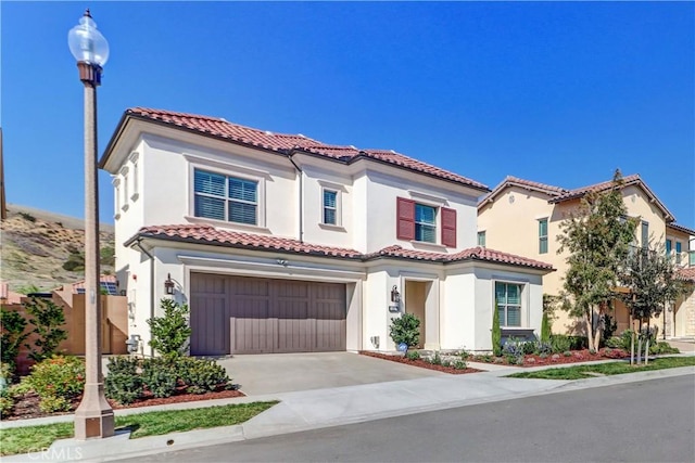 mediterranean / spanish home featuring a garage, stucco siding, concrete driveway, and a tiled roof