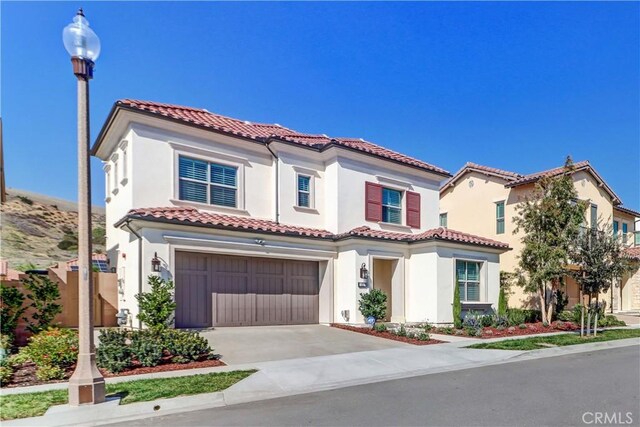 mediterranean / spanish-style home featuring concrete driveway, a tile roof, an attached garage, and stucco siding