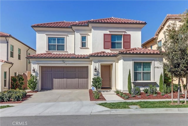 mediterranean / spanish-style home with concrete driveway, a tile roof, an attached garage, and stucco siding