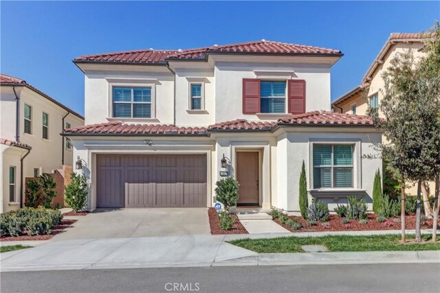 mediterranean / spanish house with a garage, concrete driveway, a tiled roof, and stucco siding