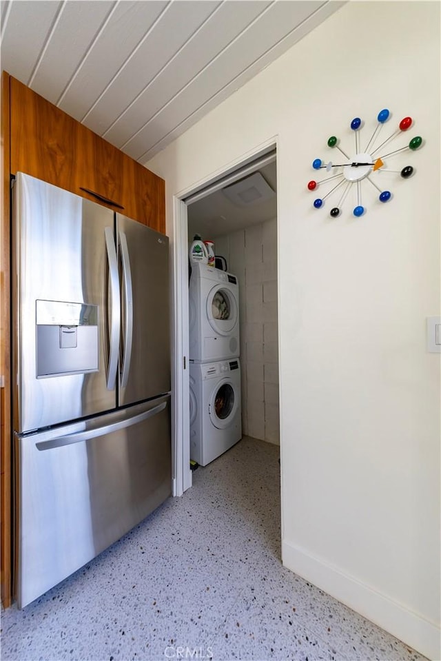 kitchen featuring brown cabinetry, stacked washer / drying machine, stainless steel refrigerator with ice dispenser, and baseboards