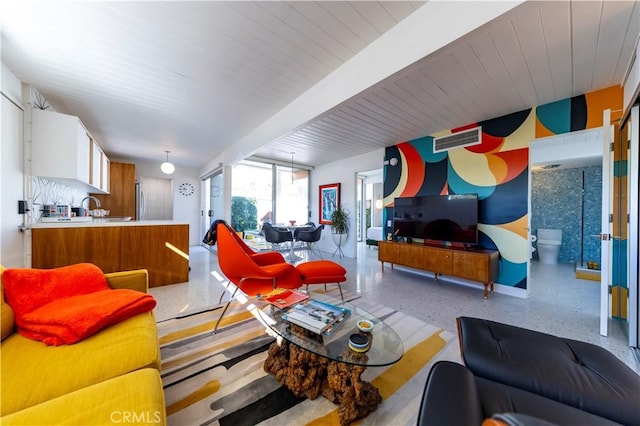 living area with light speckled floor, beam ceiling, and visible vents