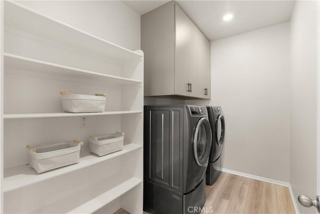 laundry area with light wood-type flooring, cabinet space, baseboards, and washing machine and clothes dryer