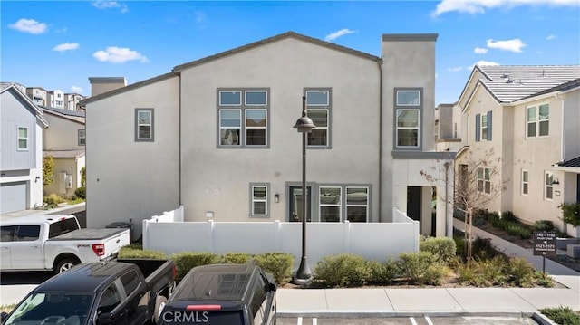view of front of house featuring stucco siding, fence, and uncovered parking