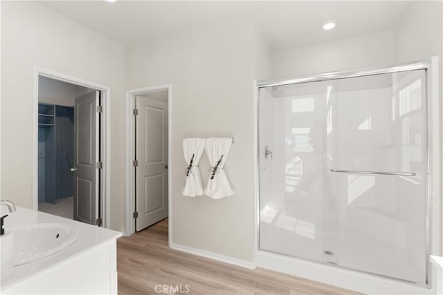 full bath featuring baseboards, a spacious closet, wood finished floors, a shower stall, and vanity