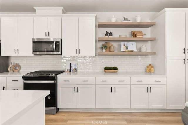 kitchen featuring light countertops, range with gas cooktop, stainless steel microwave, and white cabinets