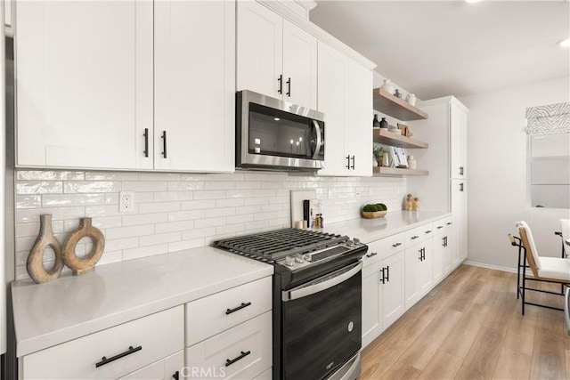 kitchen featuring stainless steel microwave, gas range oven, light countertops, light wood-style floors, and backsplash