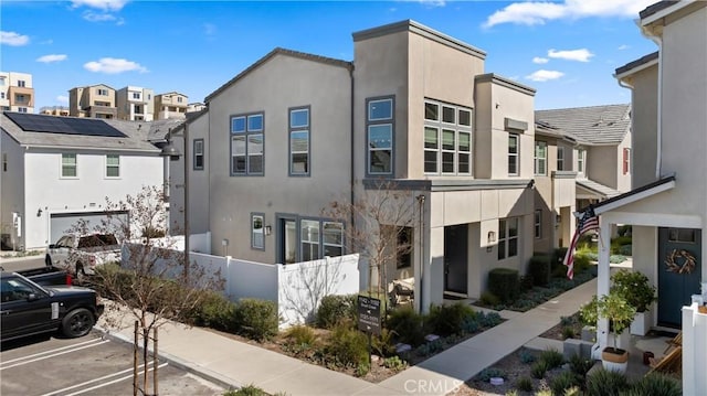 view of front of house featuring uncovered parking, an attached garage, fence, stucco siding, and a residential view