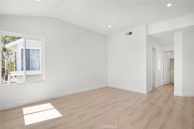 empty room featuring baseboards, visible vents, vaulted ceiling, and light wood finished floors