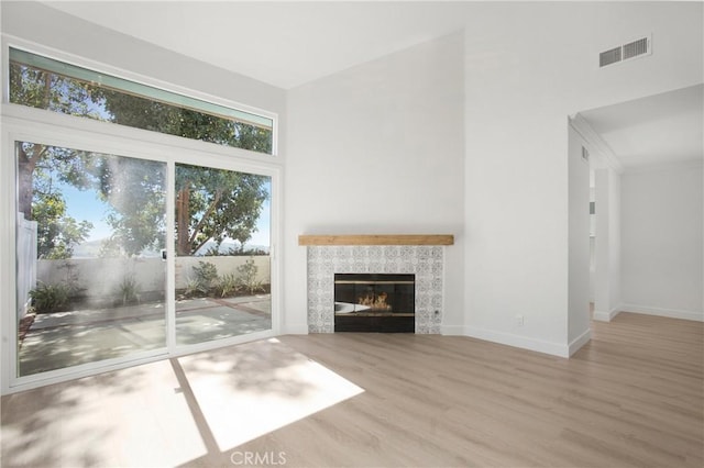 unfurnished living room featuring a tile fireplace, visible vents, baseboards, and wood finished floors