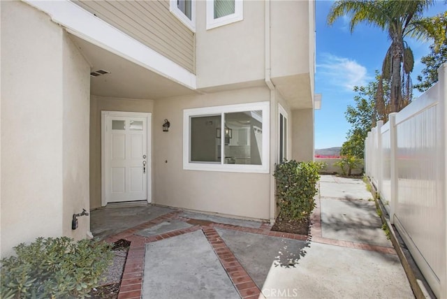 property entrance featuring a patio area, fence, visible vents, and stucco siding