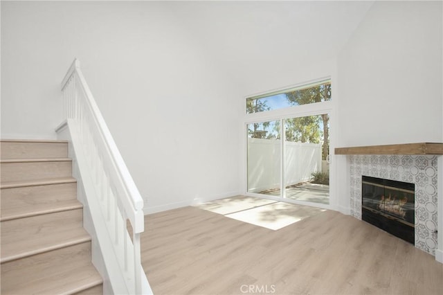 unfurnished living room featuring baseboards, a fireplace, light wood finished floors, and stairs